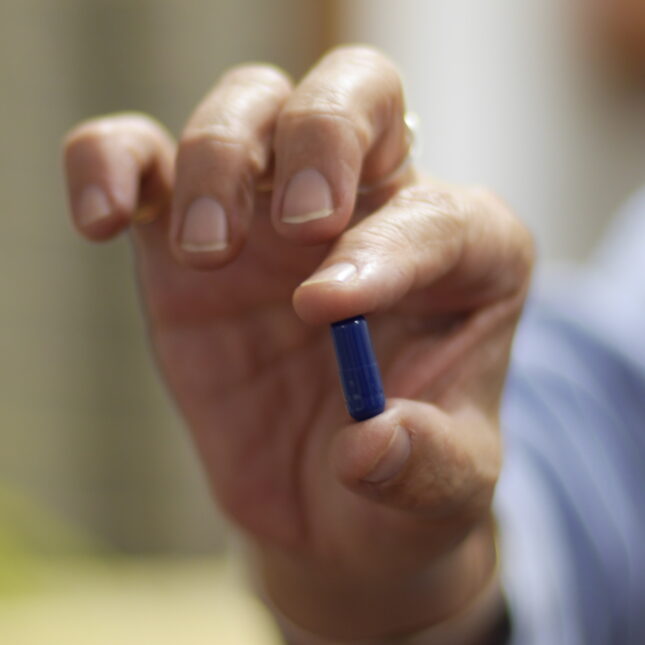 Patient holds blue pill in hand. -- health coverage from STAT