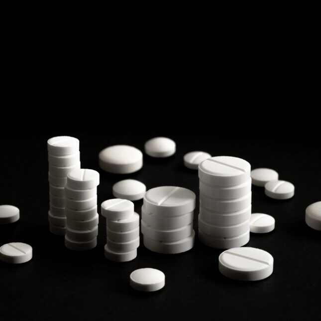 A stock photograph of round white pills stacked in piles to resemble money on a stark black background