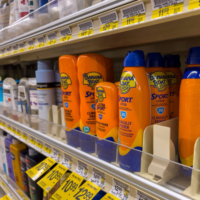 Bottles of sunscreen, most of which in orange packaging, line up on a grocery store shelf — first opinion coverage from STAT