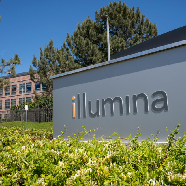 A silver sign surrounded by shrubs shows the logo of Illumina, a biotech company — biotech coverage from STAT