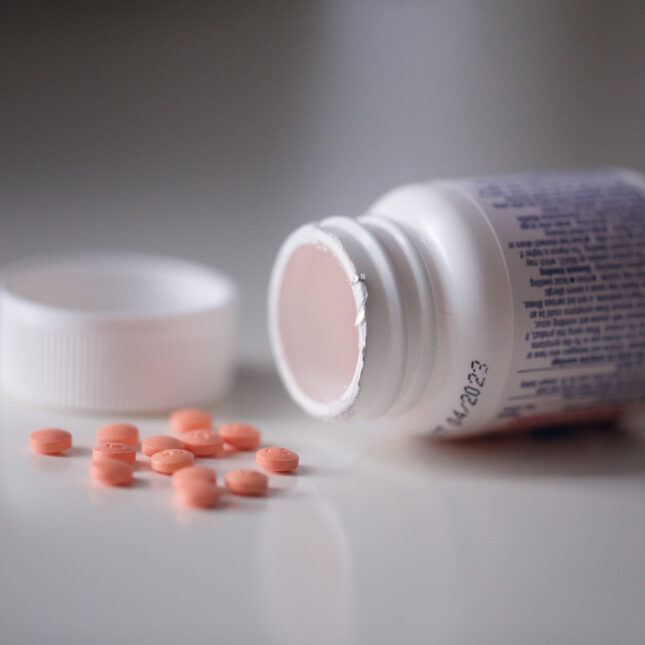 About a dozen of orange aspirin pills on the table next to its open bottle — health coverage from STAT