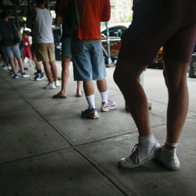 A news photo of people waiting in line to receive the Mpox vaccine before the opening of a new mass vaccination site at the Bushwick Education Campus in Brooklyn on July 17, 2022, in New York City. Photo is taken from street level and no faces are showing