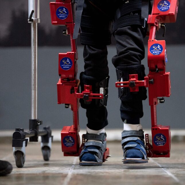 A child with cerebral palsy stands wearing robotic exoskeleton outside their black pants — health tech coverage from STAT