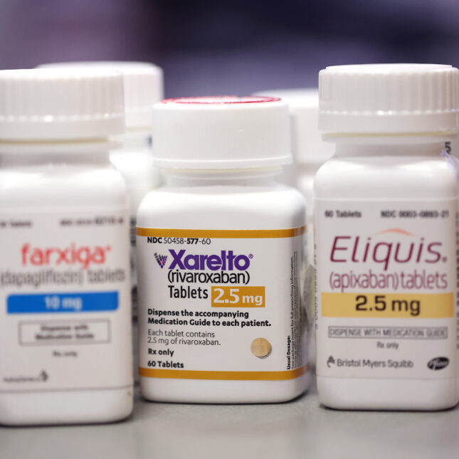 Several bottles of prescription drugs were grouped together on a table. The three on the front are Farxiga on the left, Eliquis on the right, and Xarelto in the middle and in focus — first opinion coverage from STAT