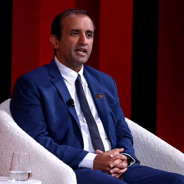 Dr. Raj Panjabi in blue suits speaks while sitting in a white chair, in front of a red backdrop during the 2024 TIME100 Summit — coverage from STAT