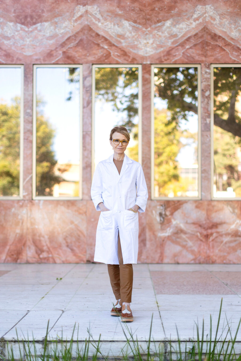 Barbara Natterson-Horowitz, a cardiologist and evolutionary biologist, poses with both hands in the pocket of a white coat, standing in front of a dark peach marble wall with five windows — Q&A coverage from STAT