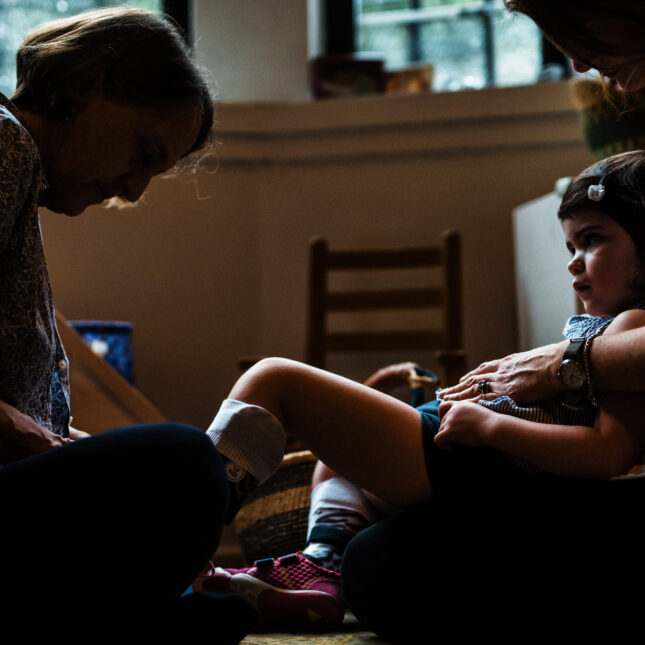 Sally Jackson, right, holds her daughter, Susannah Rosen, 3, as physical therapist, Gay Rosenberg, helps Susannah put on leg braces during a physical therapy session at Sally's home in Harlem on August 18, 2017.